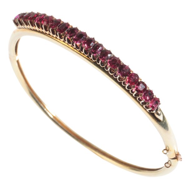 A GOLD COLOURED METAL AND RUBY HINGED BANGLE