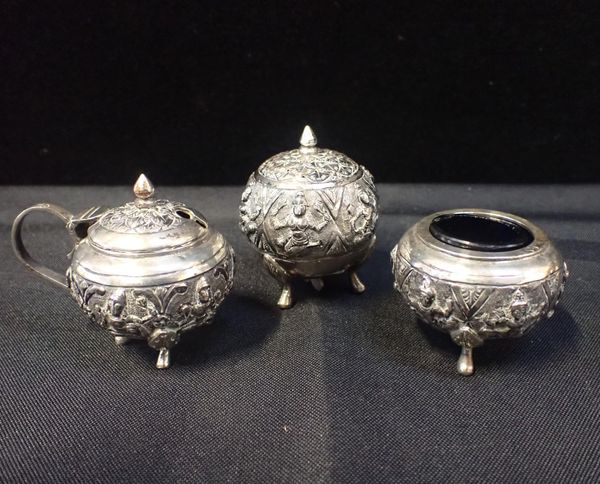 AN INDIAN KUTCH STYLE EMBOSSED WHITE METAL THREE PIECE CRUET