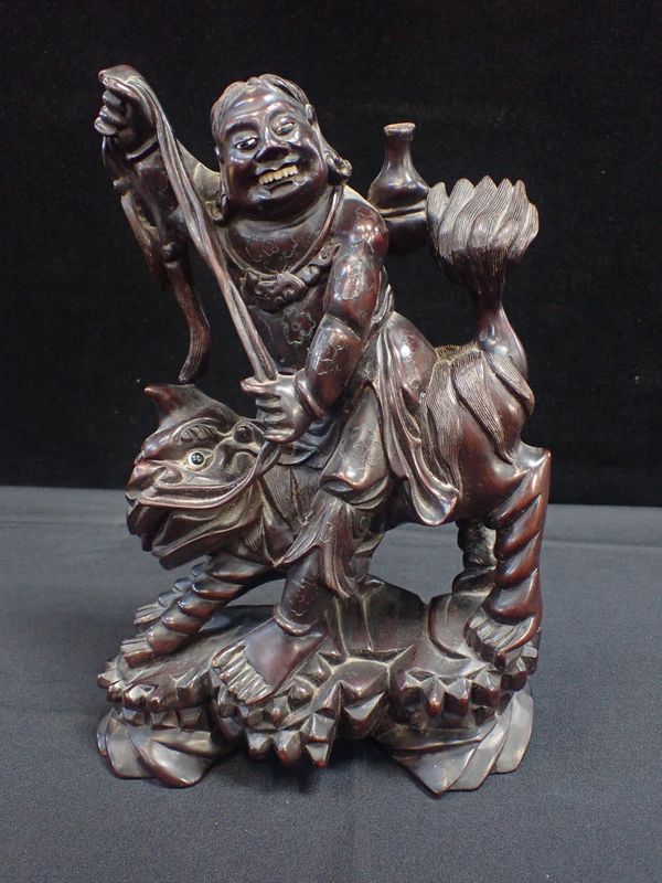 A CARVED HARDWOOD FIGURE OF AN ASIAN DEITY RIDING A LION