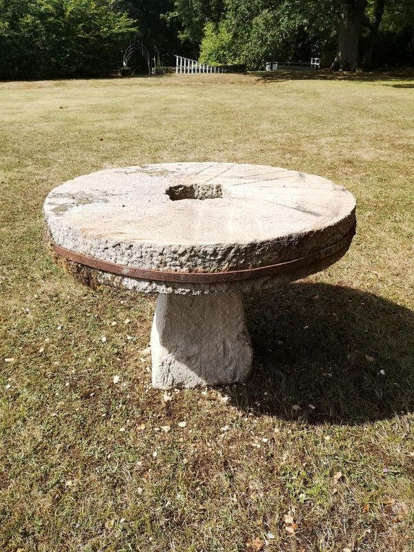 A carved stone table with millstone top on staddlestone base 107cm diameter