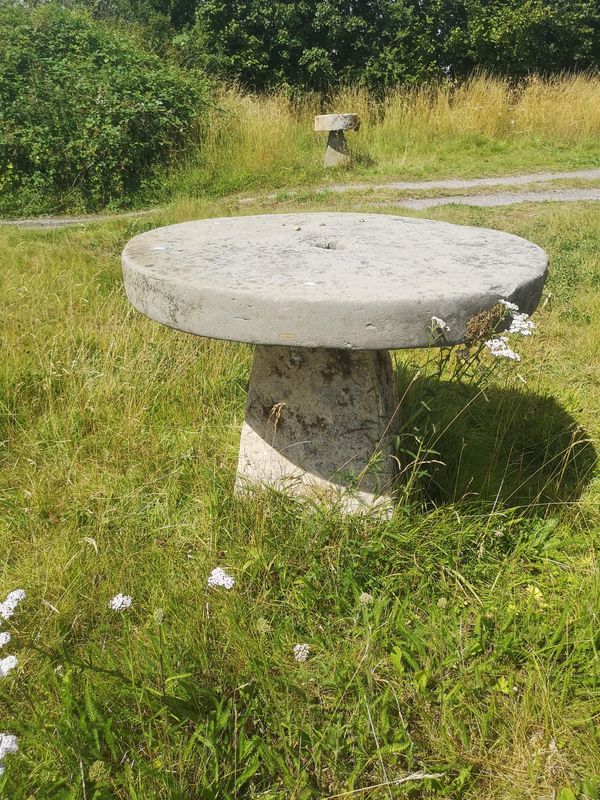 A carved stone table with millstone top on staddlestone base 80cm high by 90cm diameter