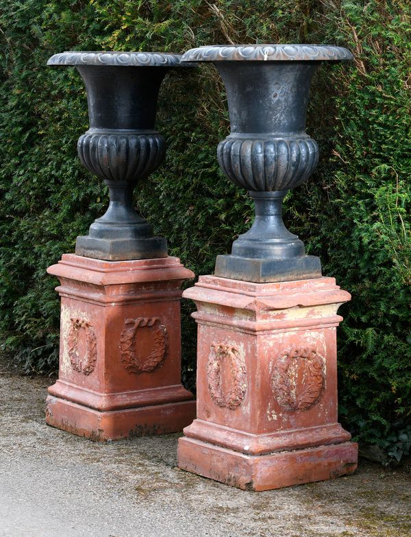 ‡ A pair of cast iron urns  modern 78cm high, on late Victorian terracotta pedestals 145cm high overall 
