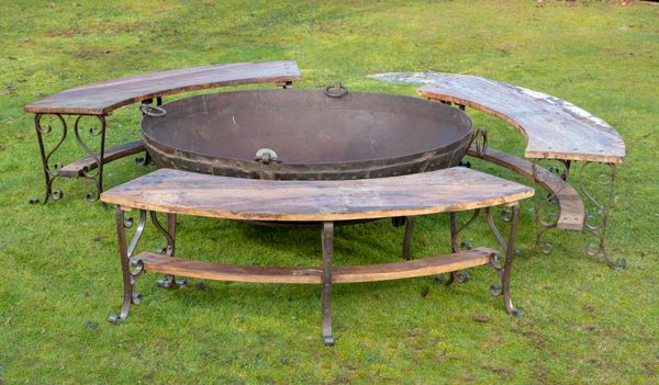 † A large wrought iron kadai on stand modern 148cm diameter, together with a set of three curved benches with wooden tops