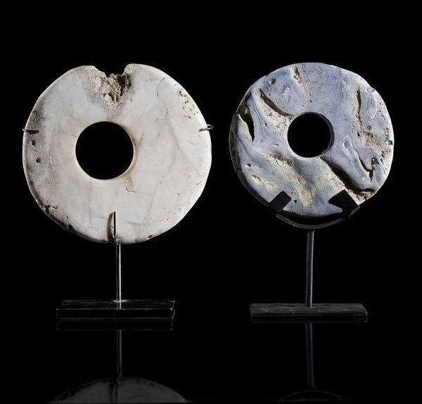 A currency disc made from clam shell on stand Oceanic 29cm high overall, together with a currency disc made from blue coral on stand, Oceanic 29cm...