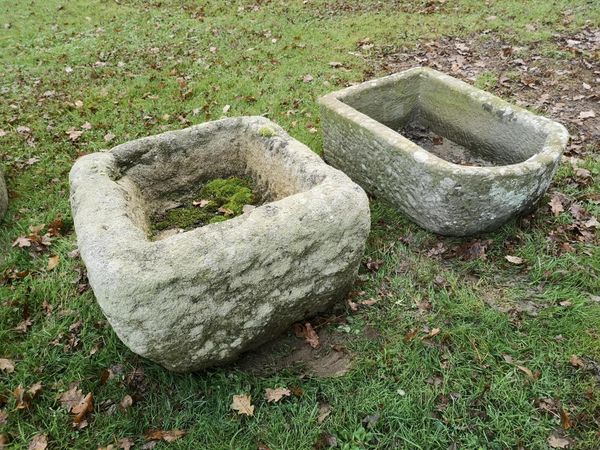 A roughly hewn rectangular stone trough 29cm high by 55cm wide by 50cm deep, together with another rounded rectangular carved stone trough, 22cm high...