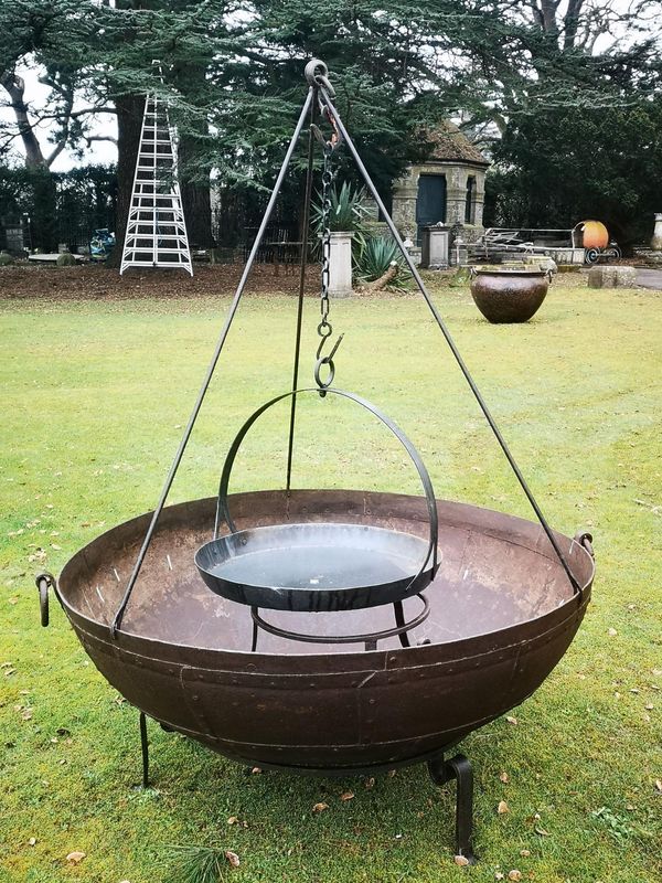 † A riveted wrought iron kadai Indian, 20th century with a later tripod and with hanging skillet 110cm diameter