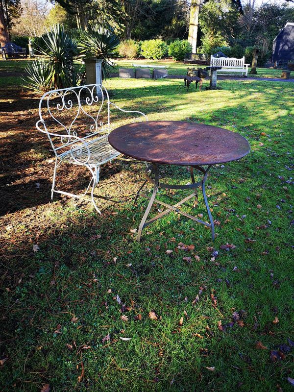 A wrought iron seat French, 1st half 20th century 123cm wide, together with a wrought iron and sheet metal table, 20th century, 100cm diameter
