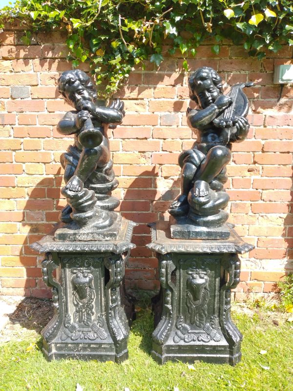 A pair of cast iron cherub musicians on pedestals
