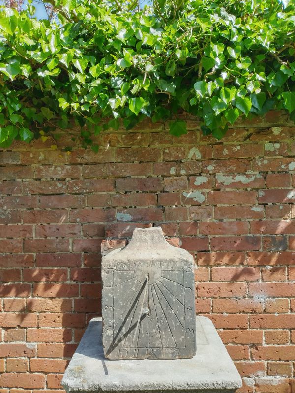 A carved red sandstone wall sundial with later copper gnomon