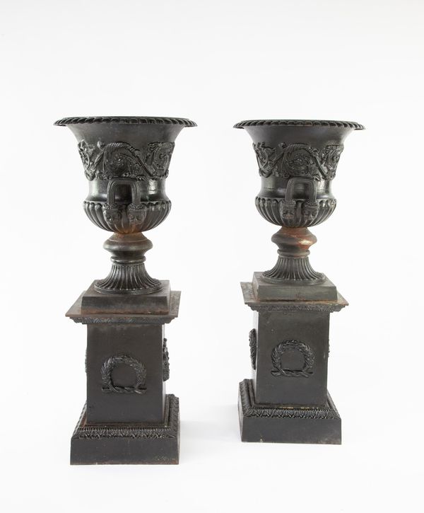 A pair of cast iron urns on pedestals