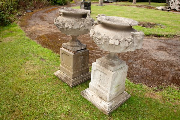 A pair of composition stone rams' head urns on pedestals