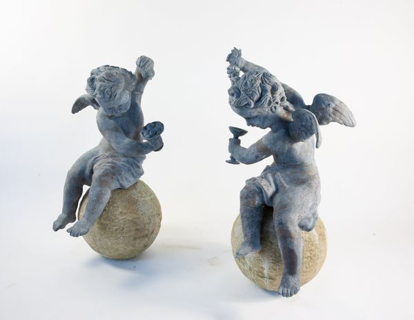 A pair of winged lead putti finials on composition stone spheres